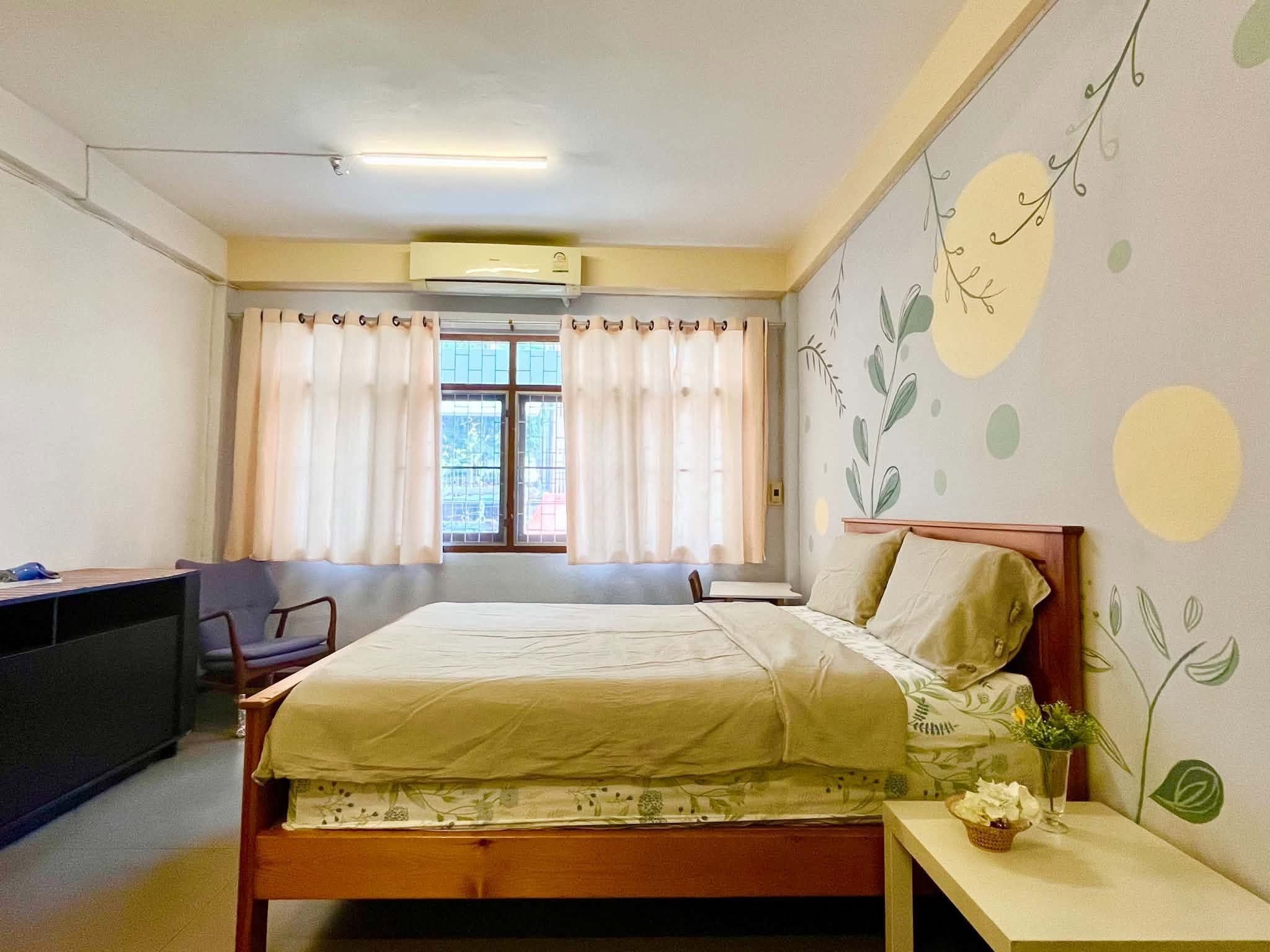 A bedroom with a bed, a desk, a chair, and a window with curtains.