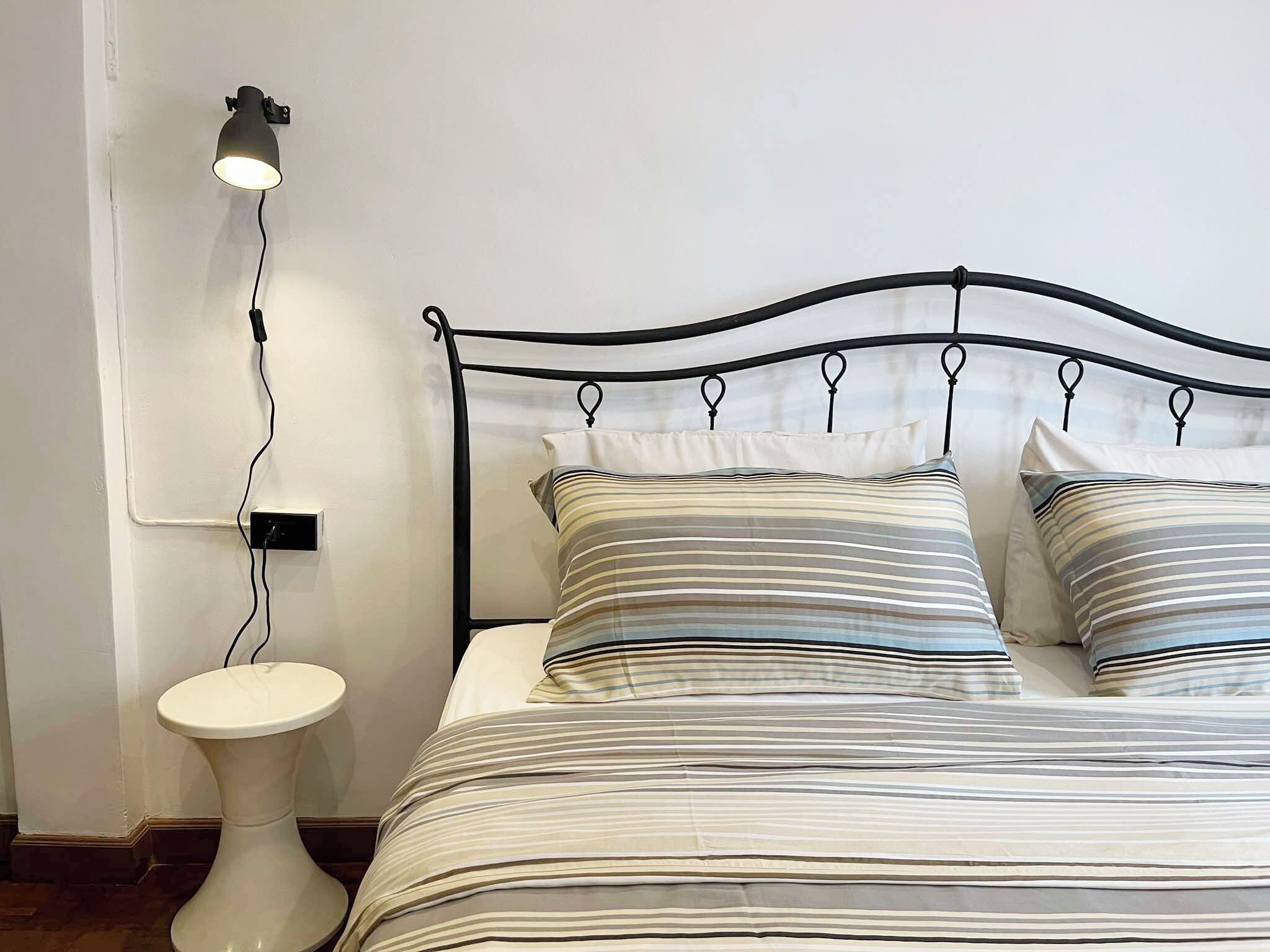 A bed with a metal frame and striped bedding, a bedside table, and a wall-mounted lamp.