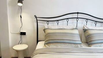 A bed with a metal frame and striped bedding, a bedside table, and a wall-mounted lamp.