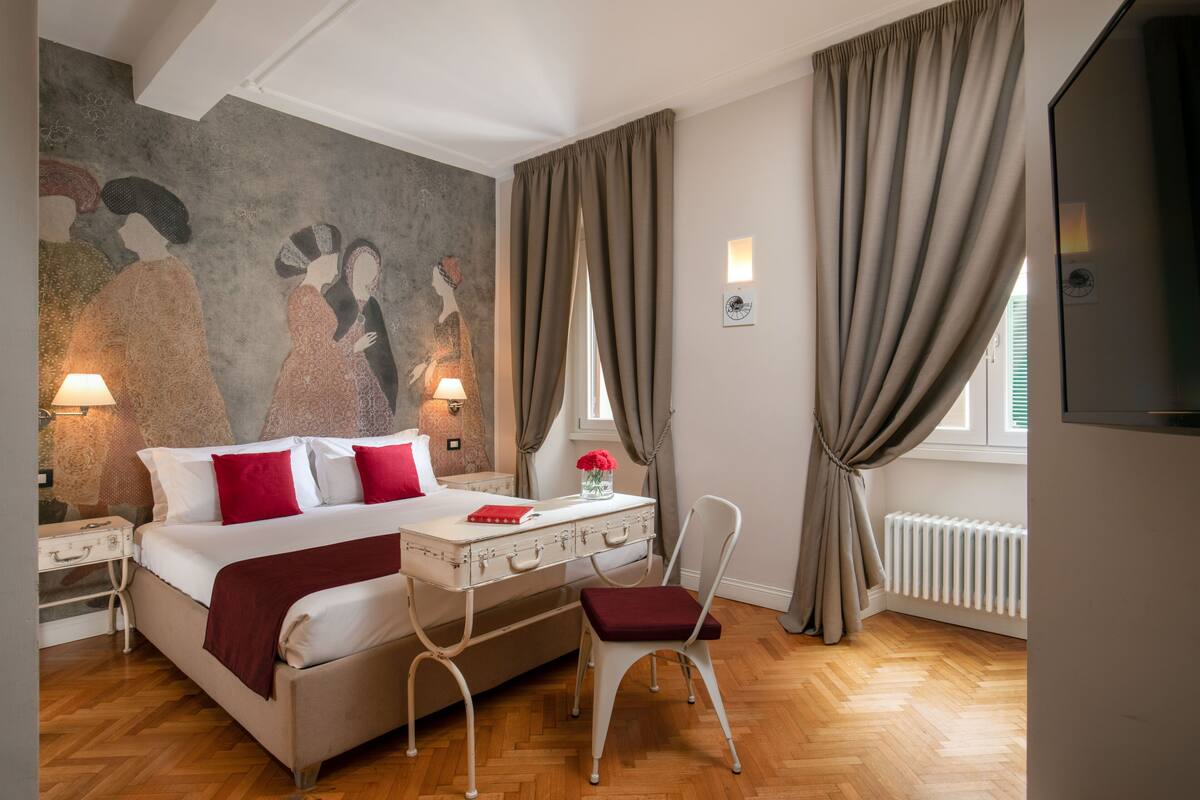 A bedroom with a bed, bedside tables, a desk, a chair, a radiator, and a wall with a mural.