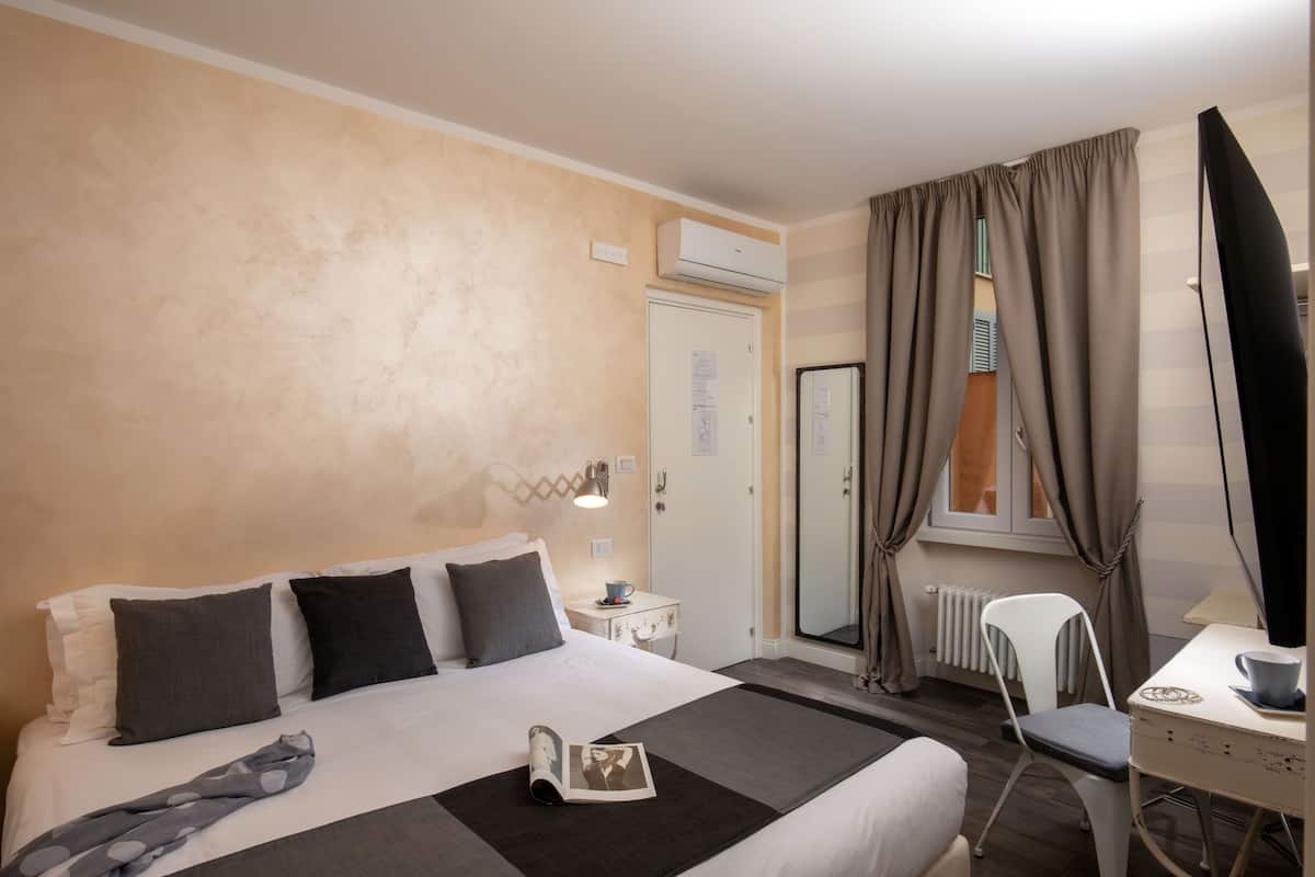 A hotel room with a bed, bedside table, lamp, chair, and a desk with a chair.