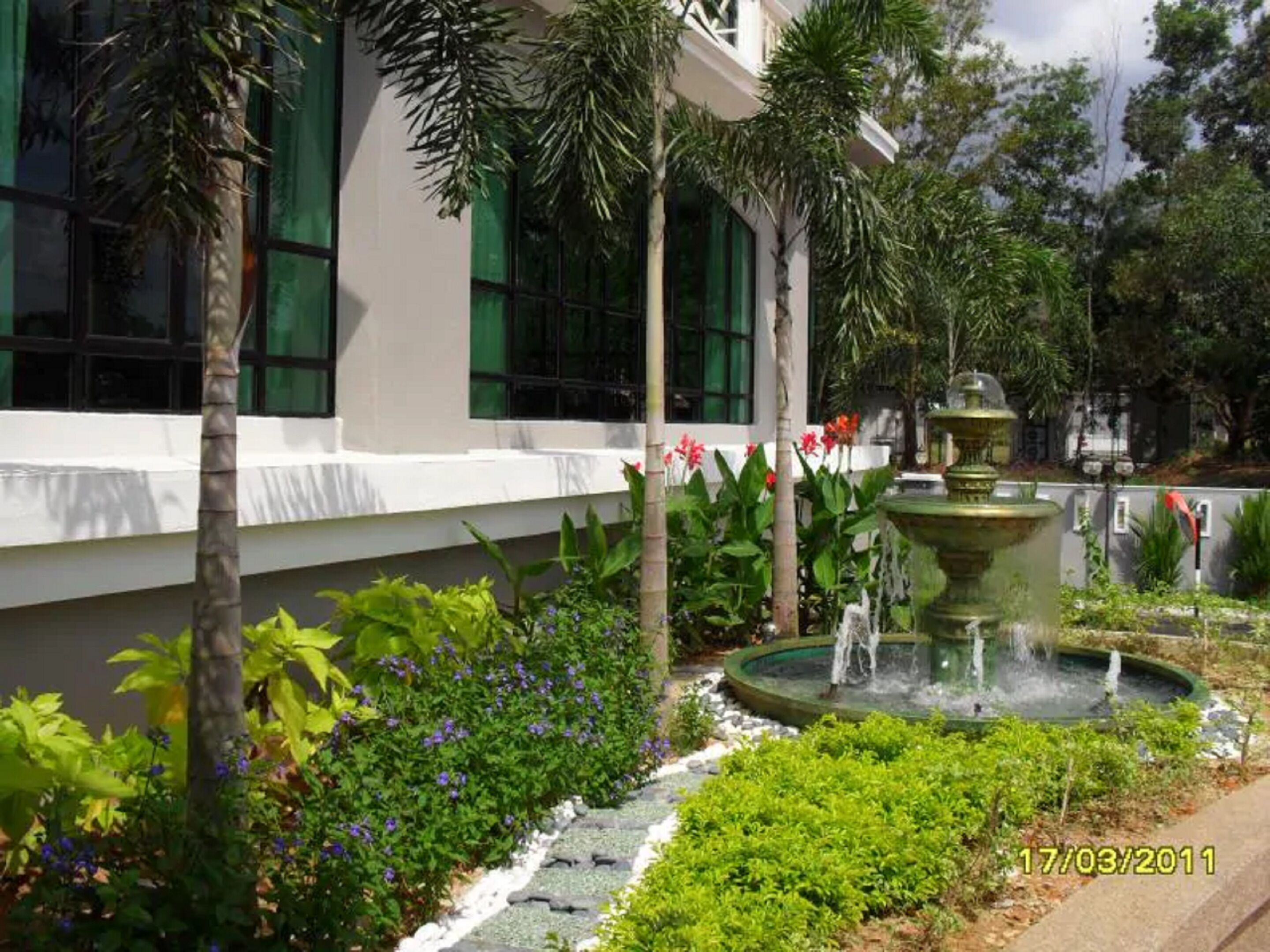 A garden with a fountain, palm trees, and a building with large windows.