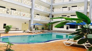 A multi-level indoor pool area with a tiled floor, lounge chairs, and potted plants. - Sutera Hotel (Seremban)