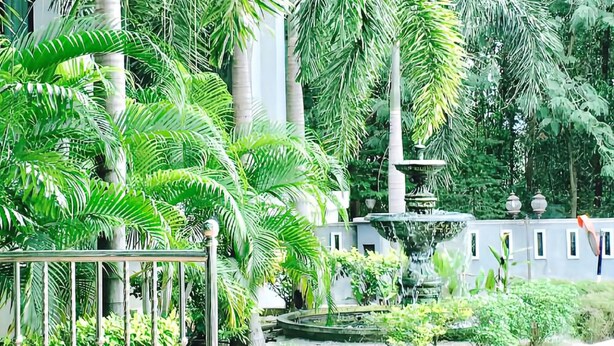 A lush garden with a central fountain, surrounded by tall palm trees and various other greenery. - Sutera Hotel (Seremban)