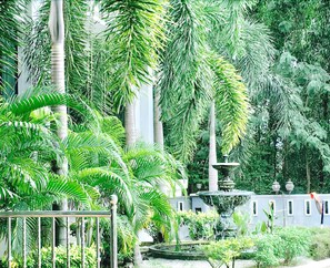 A lush garden with a central fountain, surrounded by tall palm trees and various other greenery. - Sutera Hotel (Seremban)