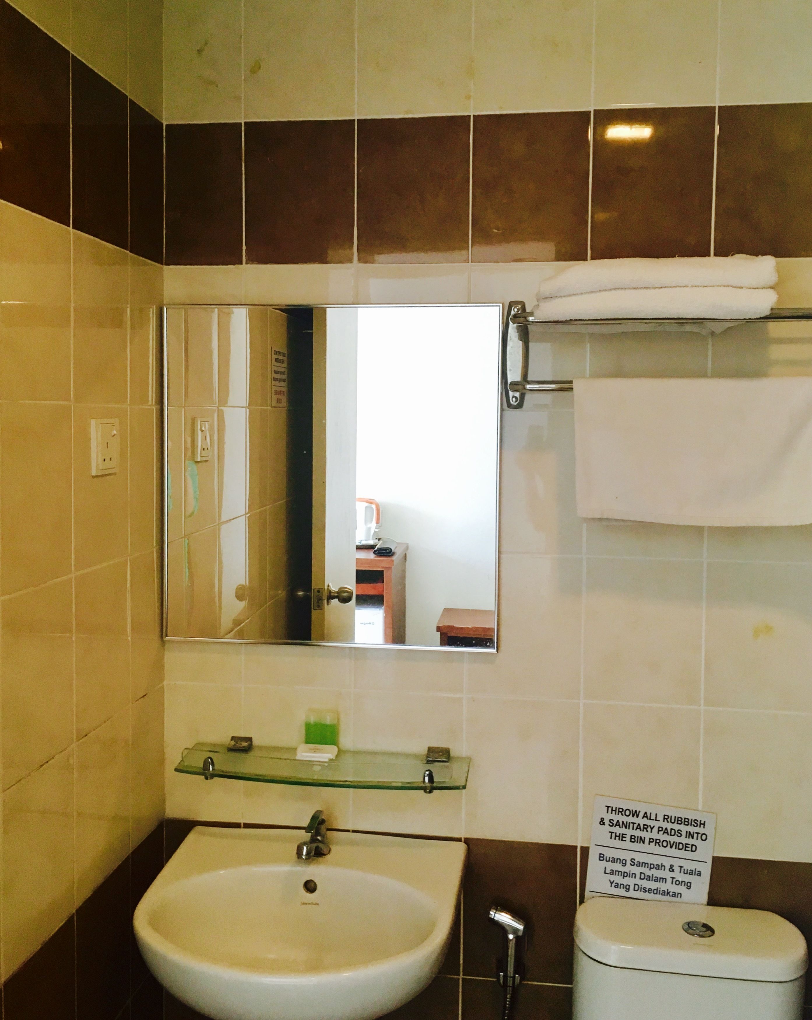 A bathroom with a sink, mirror, and toilet. There is a sign instructing to throw all rubbish into the bin.