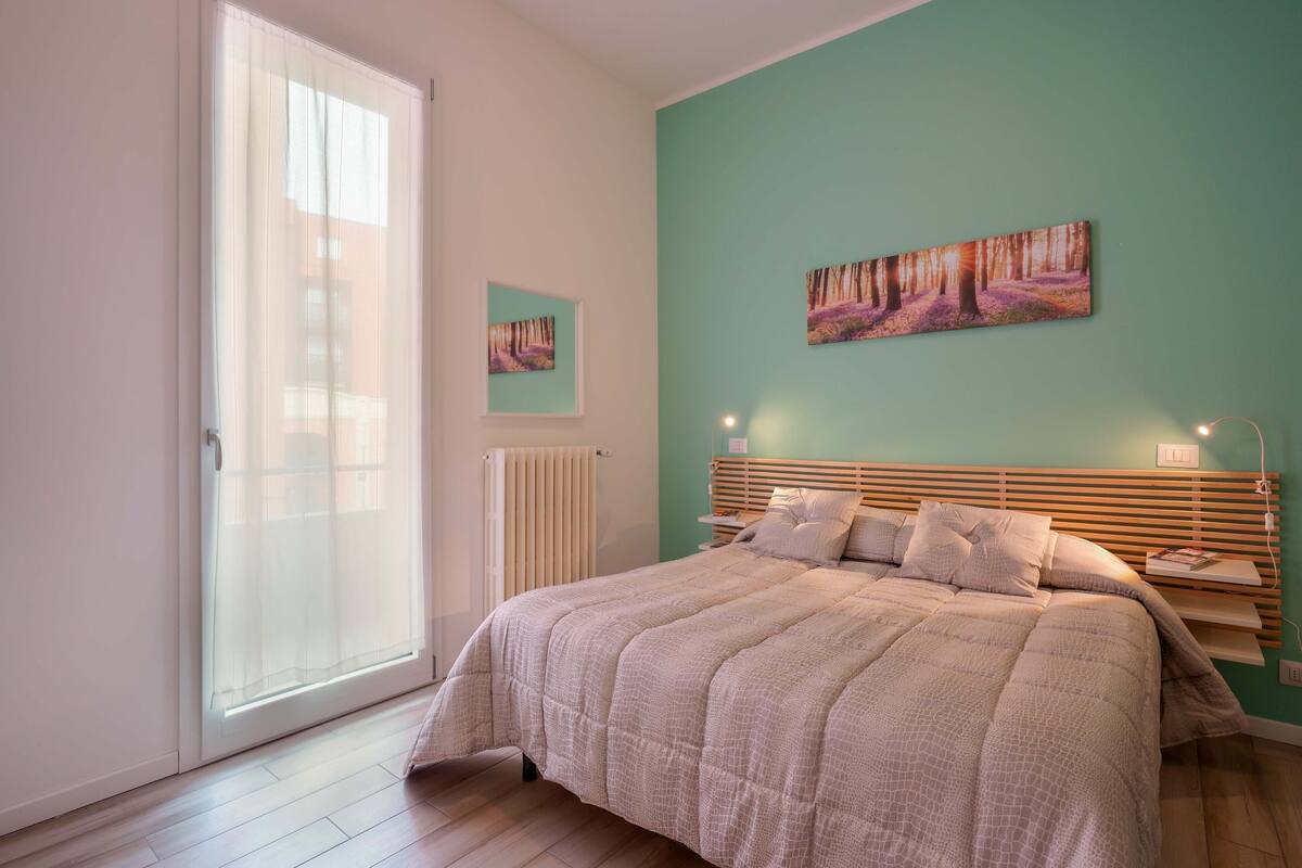 Una camera da letto con un letto, una finestra con persiane, un termosifone e un'opera d'arte appesa al muro.