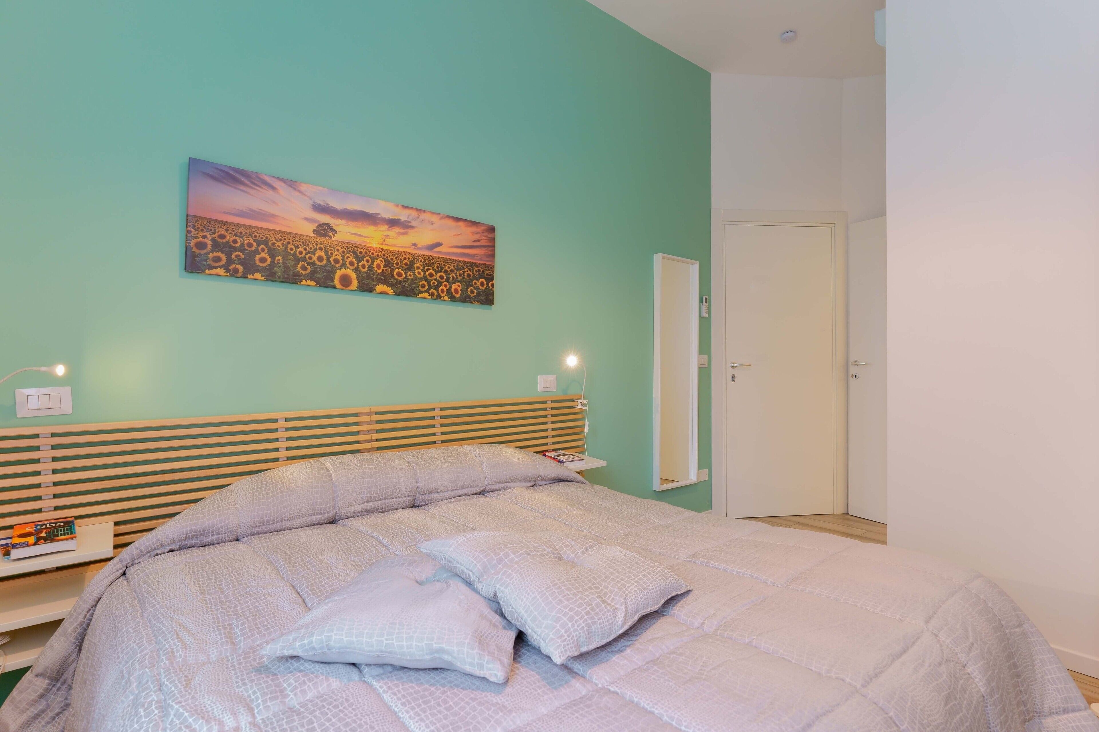 A bedroom with a bed, a nightstand, a wall-mounted painting, and a door.