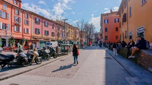 A street lined with colorful buildings, a pedestrian, and parked scooters. - B&B Bentivogli (Bologna)