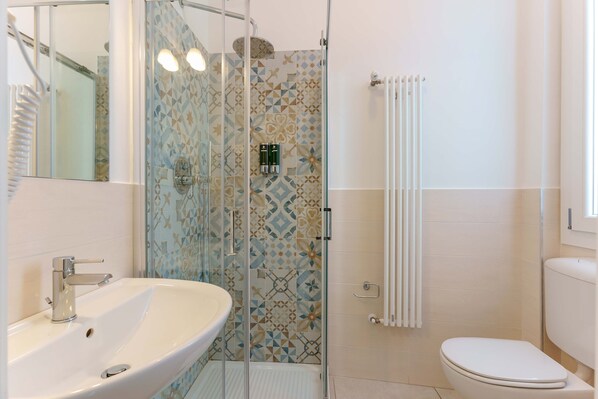 Un baño con ducha de vidrio, lavamanos blanco y retrete.