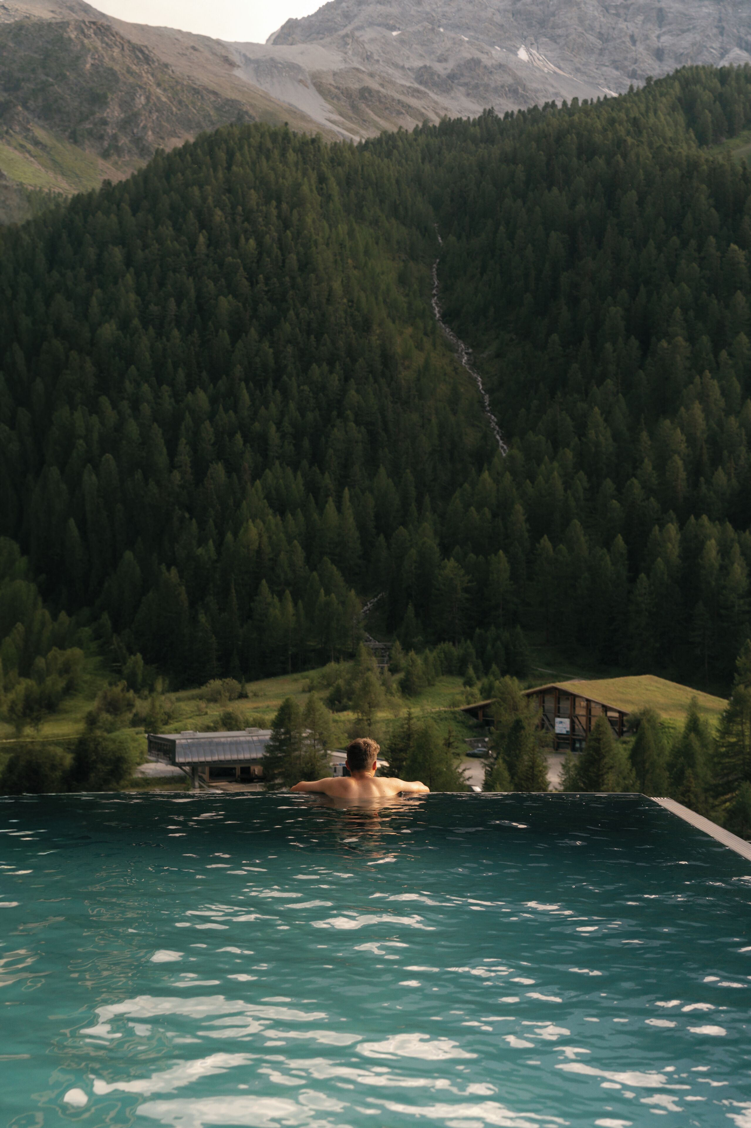 A person in a swimming pool with a mountain and forest in the background.