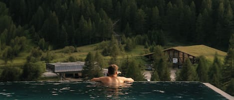 Una persona en una piscina, con una montaña y un bosque al fondo.