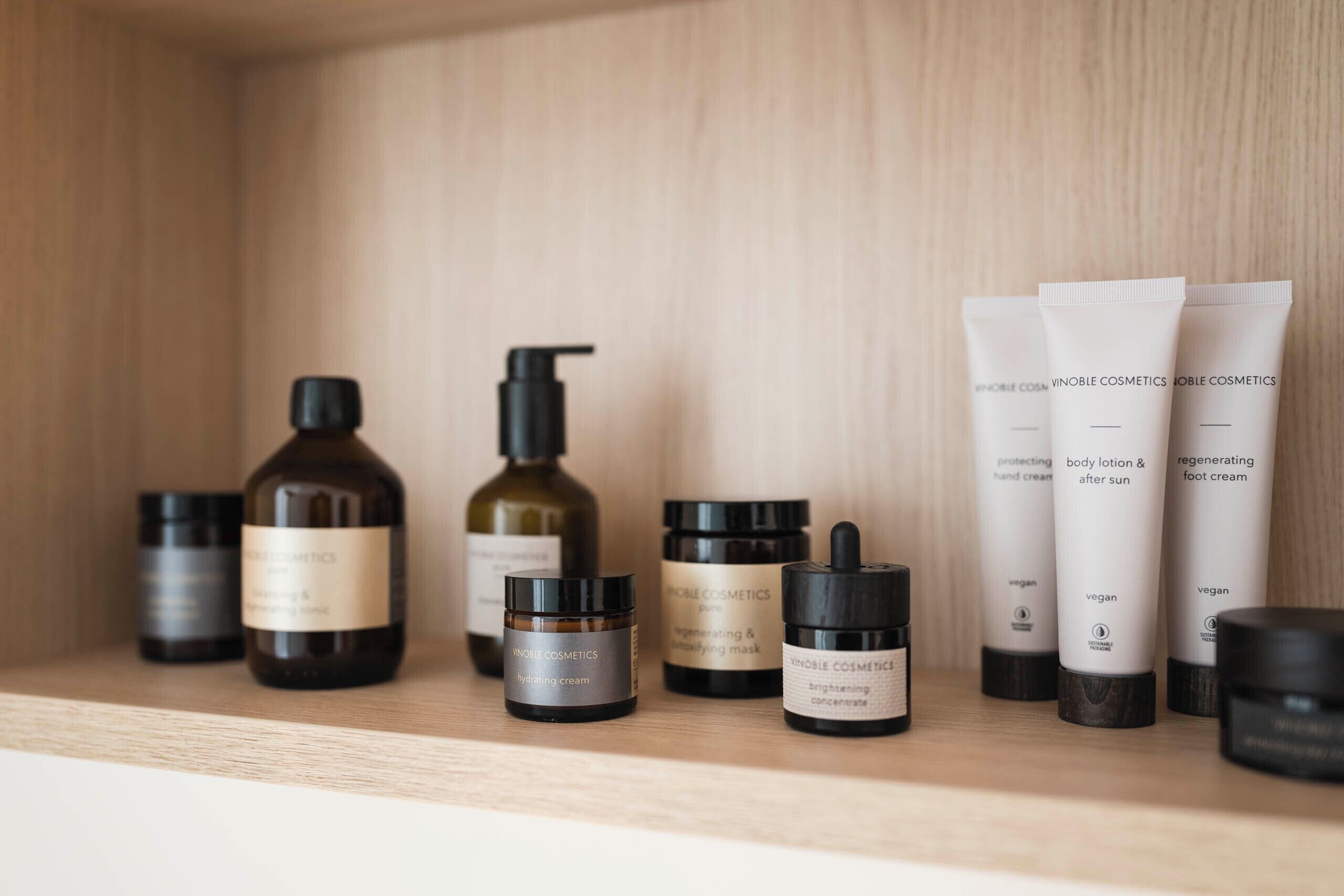 Une étagère en bois sur laquelle sont disposés divers produits de soins pour la peau de la marque VinoBelle Cosmetics.