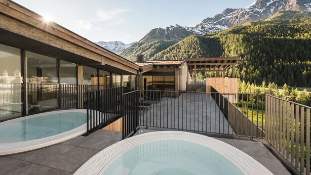 A modern building with a pool area, large windows, and a mountainous backdrop. - MyPARADIES (Stelvio)