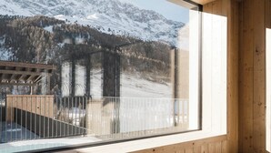 A wooden interior with a large window overlooking a snowy mountain landscape. - MyPARADIES (Stelvio)