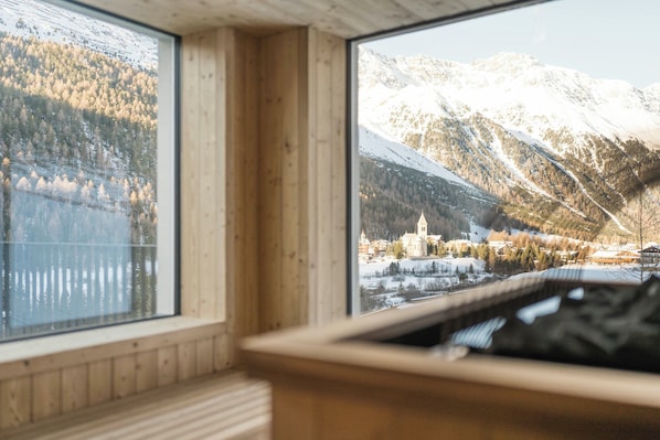 A wooden cabin with large windows offering views of a snowy mountain landscape and a lake.