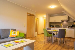 Un espacio habitable compacto con sofá, mesa de comedor, sillas, kitchenette y una puerta de madera.