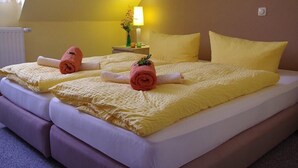 A double bed with yellow linens and rolled towels, a bedside table with a lamp, and a window with a view of the sky. - Pension & FeWo's Talblick (Eibenstock)