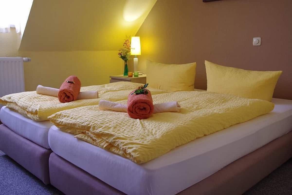 A double bed with yellow linens and rolled towels, a bedside table with a lamp, and a window with a view of the sky.