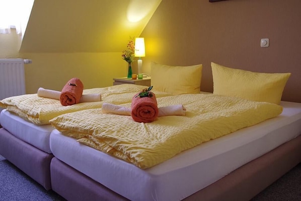 Una cama doble con sábanas amarillas y toallas enrolladas, una mesita de noche con lámpara y una ventana con vista al cielo.