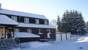A two-story house with a snow-covered roof and steps leading to the entrance. - Pension & FeWo's Talblick (Eibenstock)