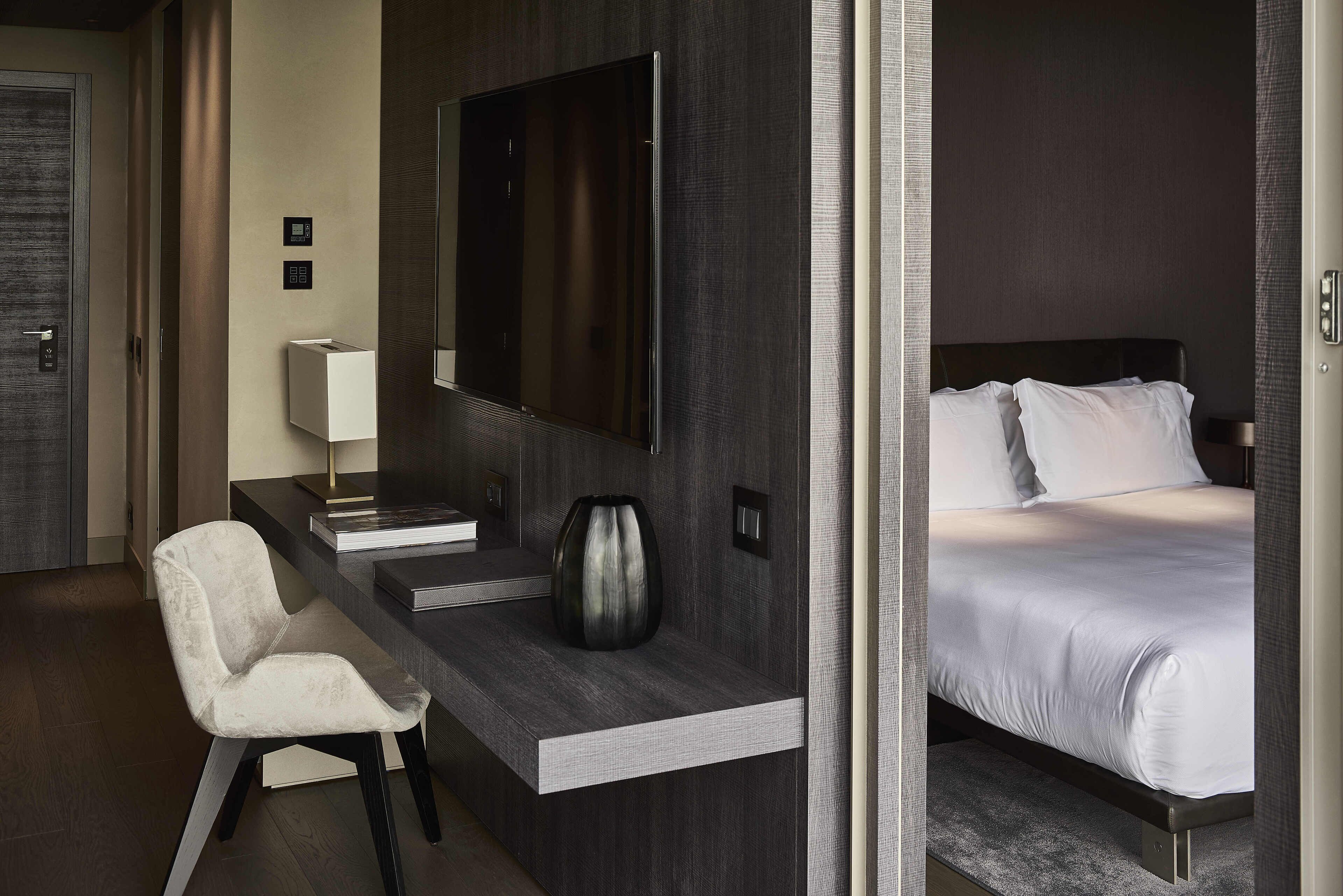 Une chambre d’hôtel comprenant un lit, un bureau avec une chaise, un téléviseur à écran plat et un vase.