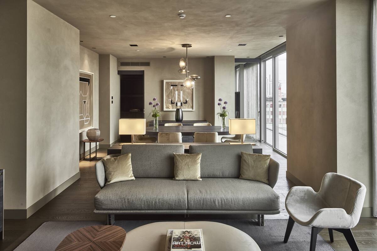 Un soggiorno moderno con un divano grigio, una poltrona bianca e un tavolino. C'è una zona pranzo con tavolo e sedie, e un'ampia finestra che offre vista sulla città.