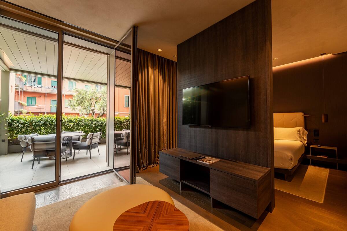Una camera d'albergo moderna con una grande TV, un letto, un divano e un balcone con mobili da esterno.
