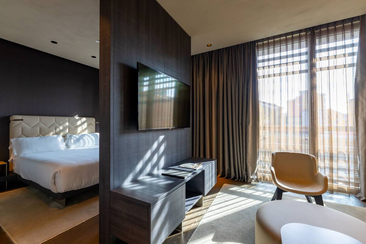 Una camera d'hotel moderna con un letto grande, una TV a parete, una scrivania e una sedia.