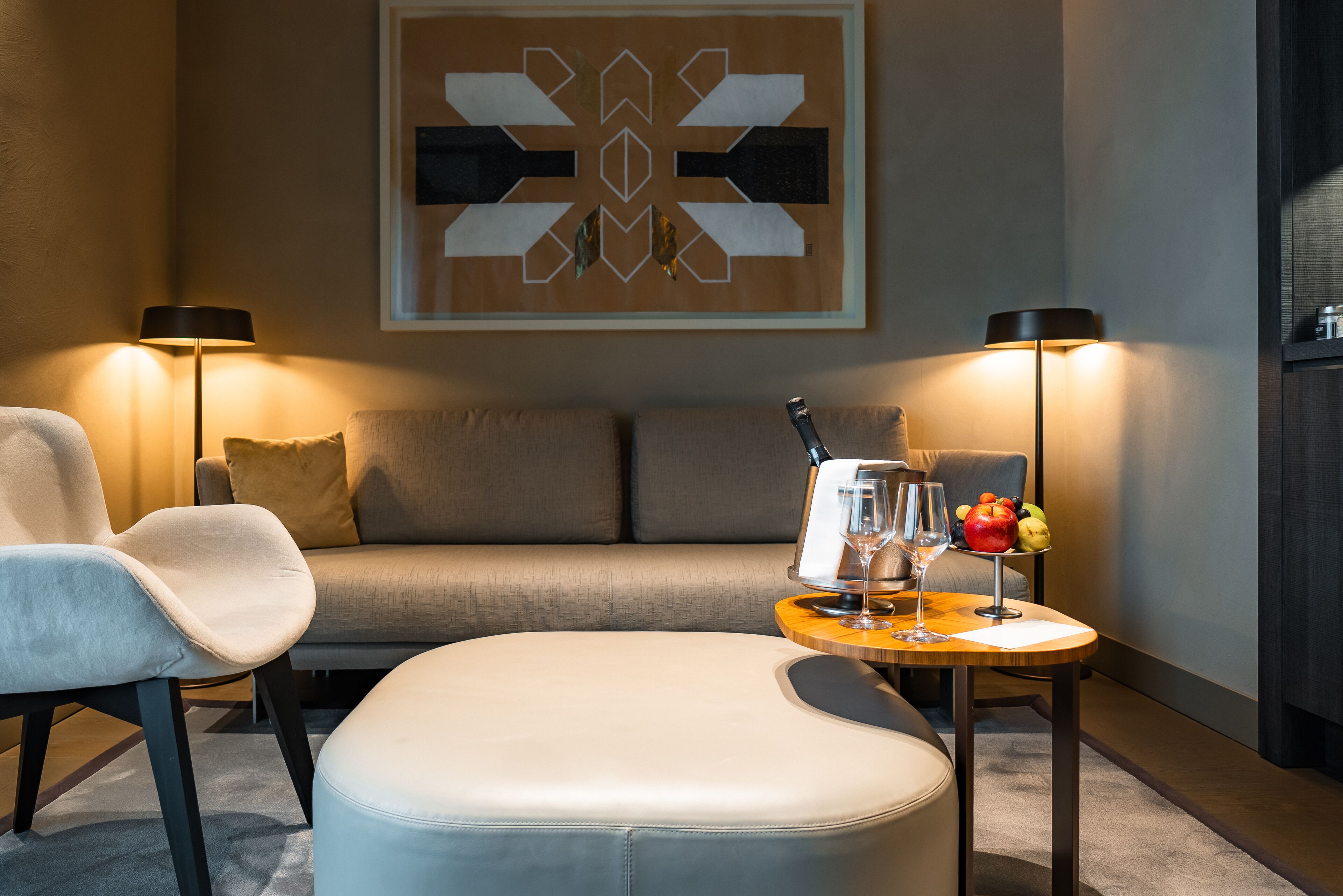 Ein modernes Wohnzimmer mit einer Couch, einem Sessel, einem kleinen Tisch mit einem Glas und einer Obstschale.