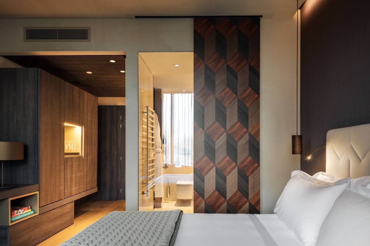 Una camera d'albergo moderna con un letto, una TV, un armadio e un bagno visibile tramite una porta di vetro.