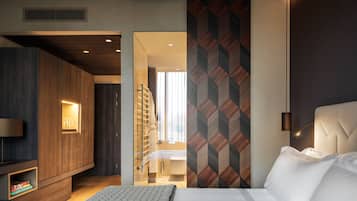 Ein modernes Hotelzimmer mit Bett, Fernseher, Kleiderschrank und sichtbarem Badezimmer hinter einer Glastür.