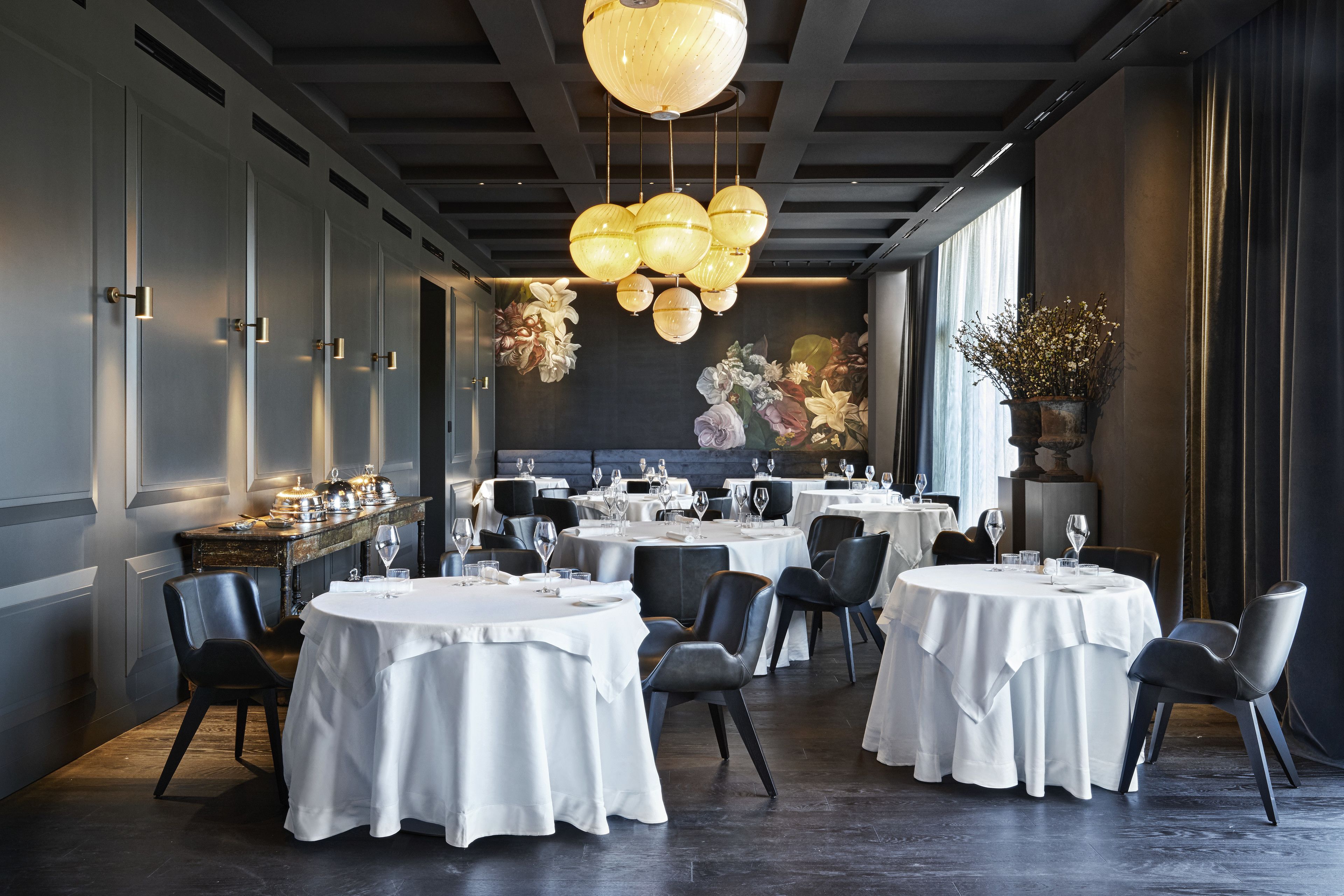 Een restaurant met ronde tafels, zwarte stoelen en een decoratieve plafondlamp.