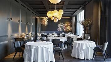 Een restaurant met ronde tafels, zwarte stoelen en een decoratieve plafondlamp.