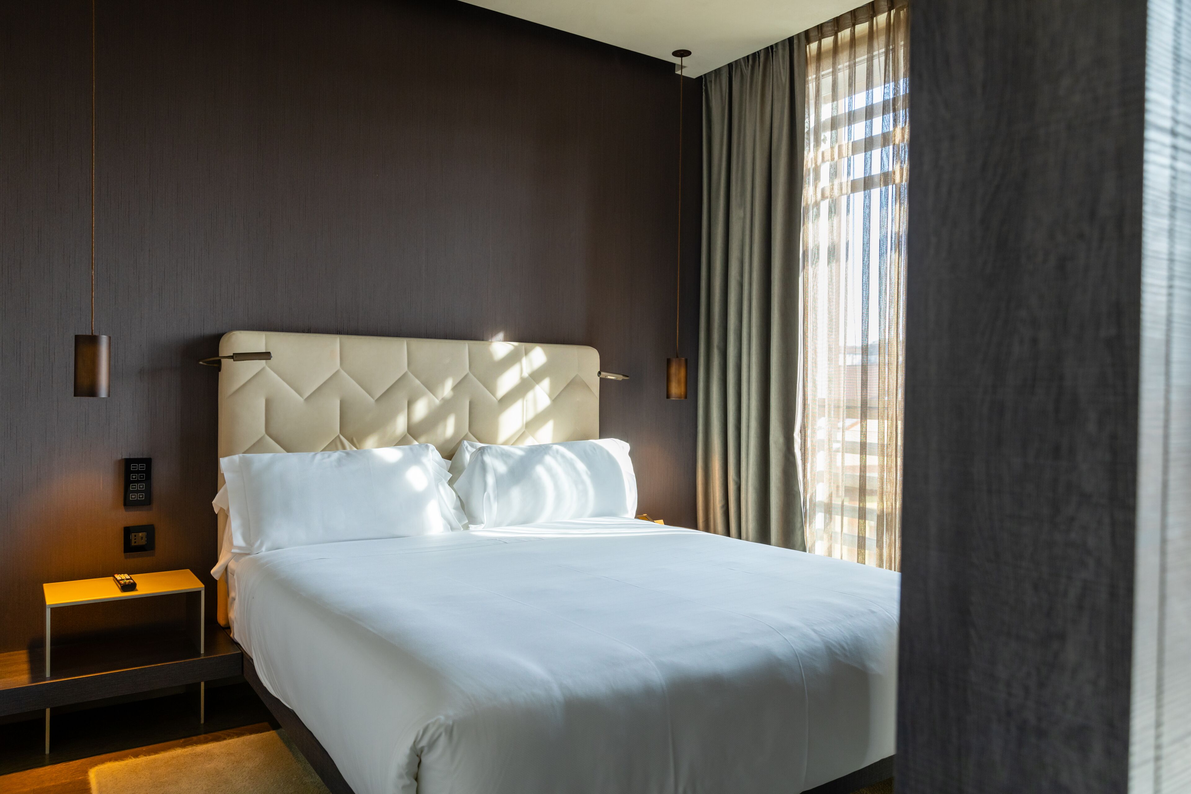 Een moderne hotelkamer met een groot bed, een nachtkastje en een raam met gordijnen.