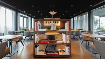 A modern library with bookshelves, tables, and chairs arranged for reading and dining.