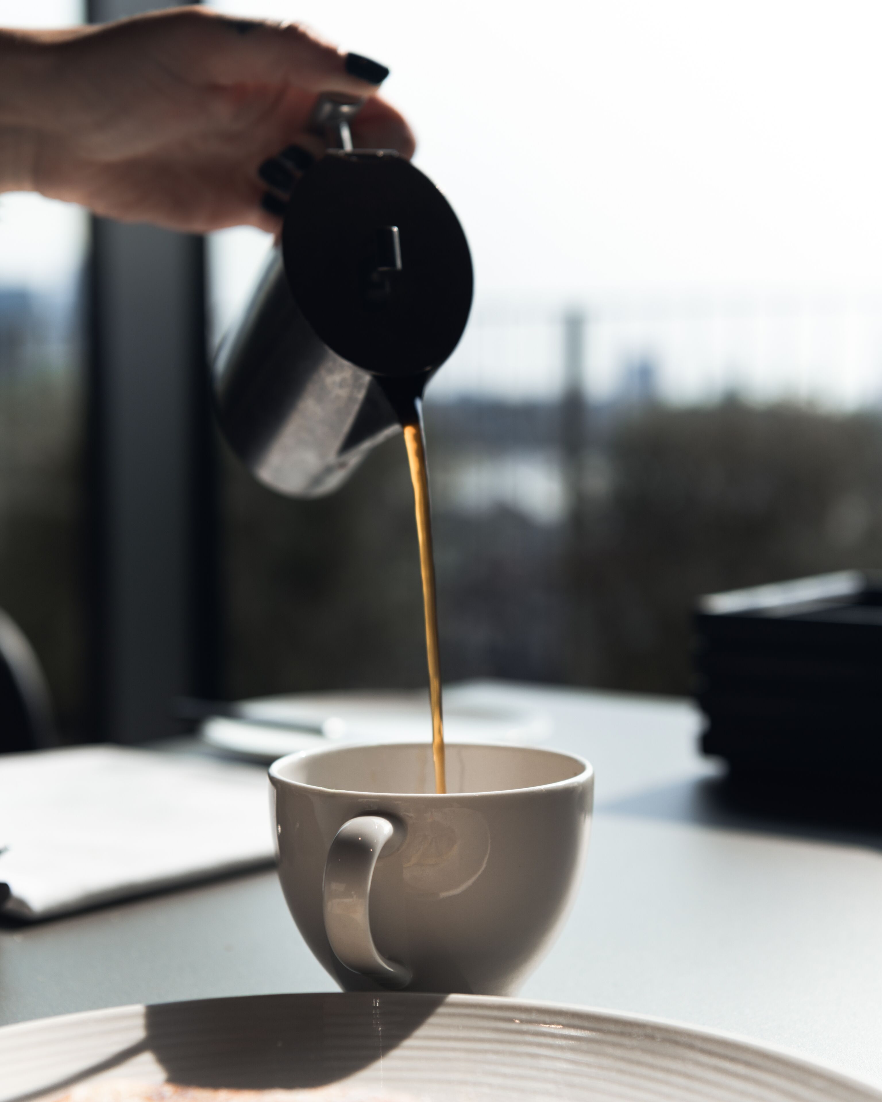 A hand pouring coffee into a cup on a table.