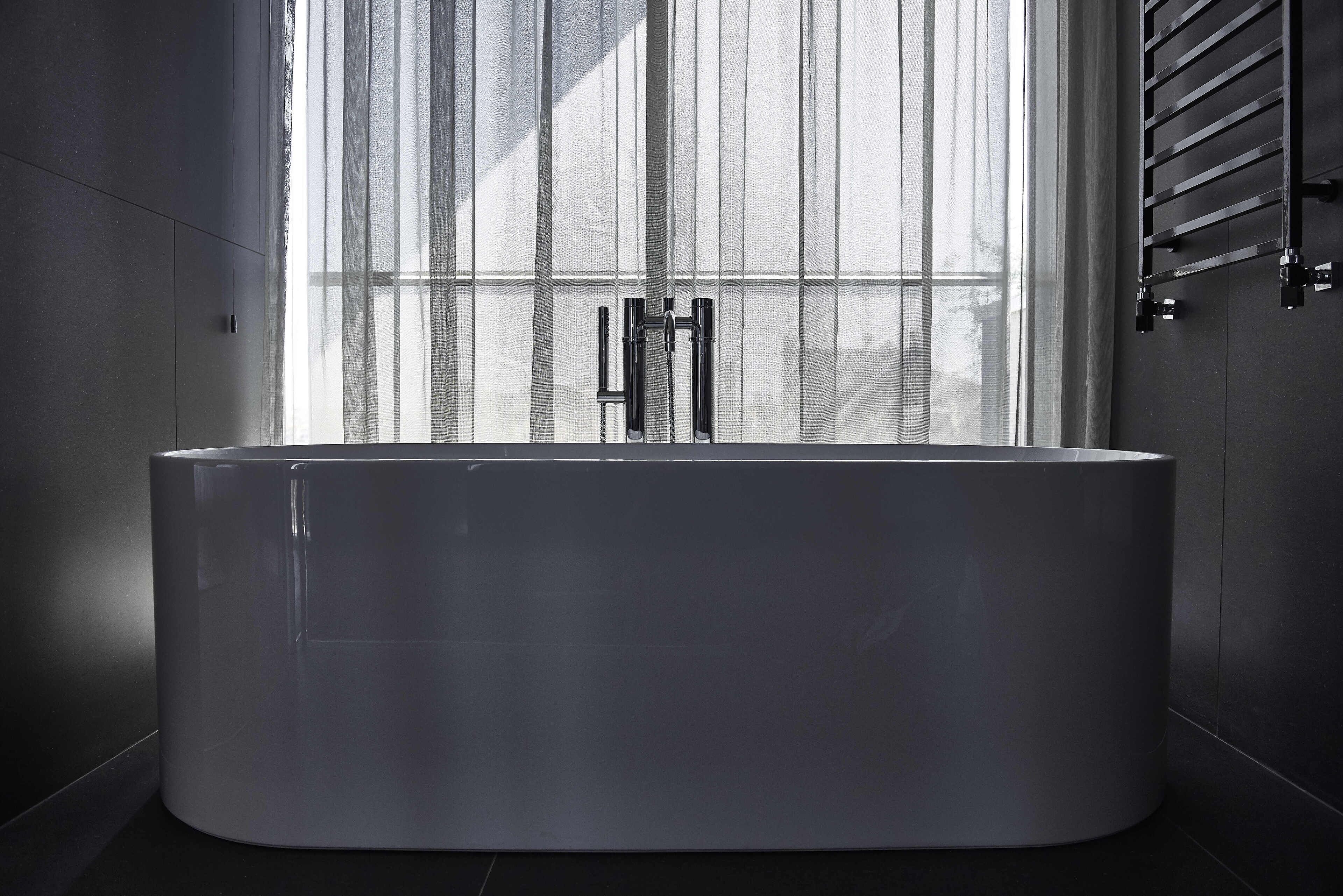 Un bagno moderno con una vasca da bagno grande, una finestra con tende leggere e un porta asciugamani.