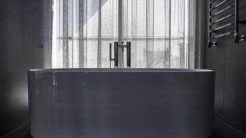 Un bagno moderno con una vasca da bagno grande, una finestra con tende leggere e un porta asciugamani.