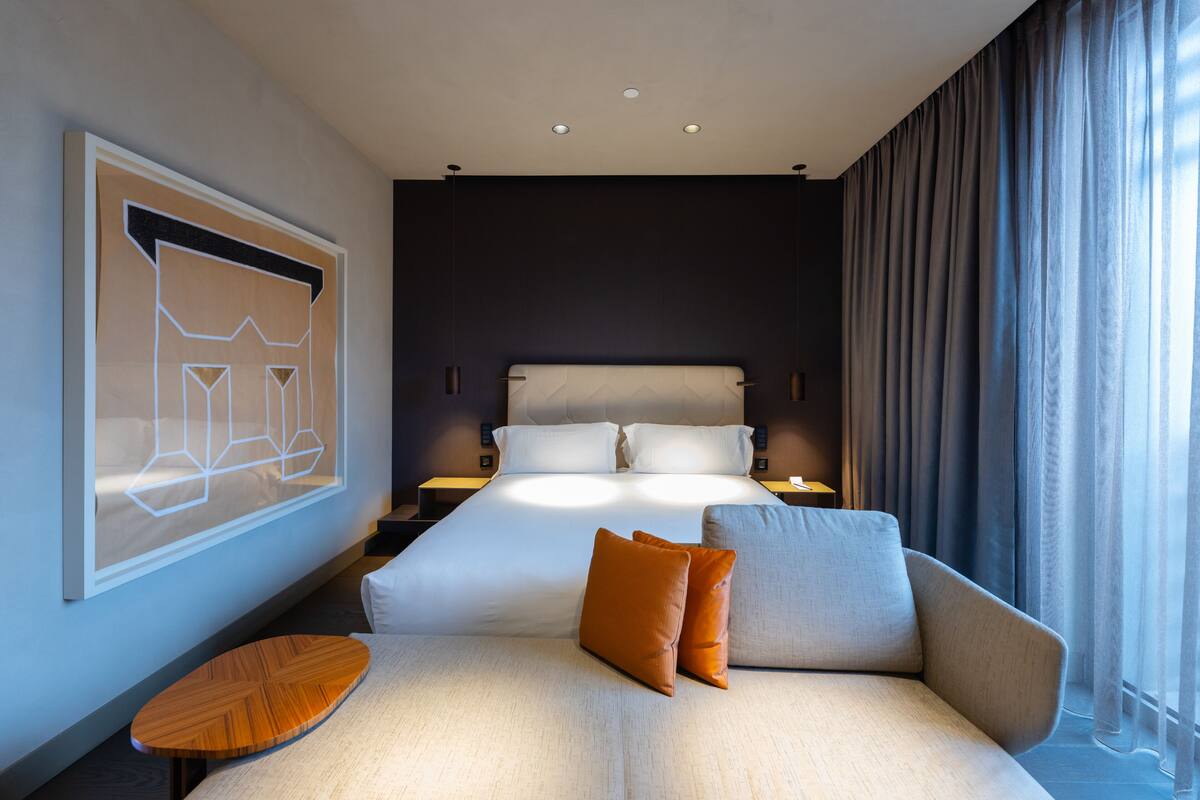 Una camera d'albergo moderna con un letto grande, un divano, un piccolo tavolo in legno e un quadro appeso al muro.