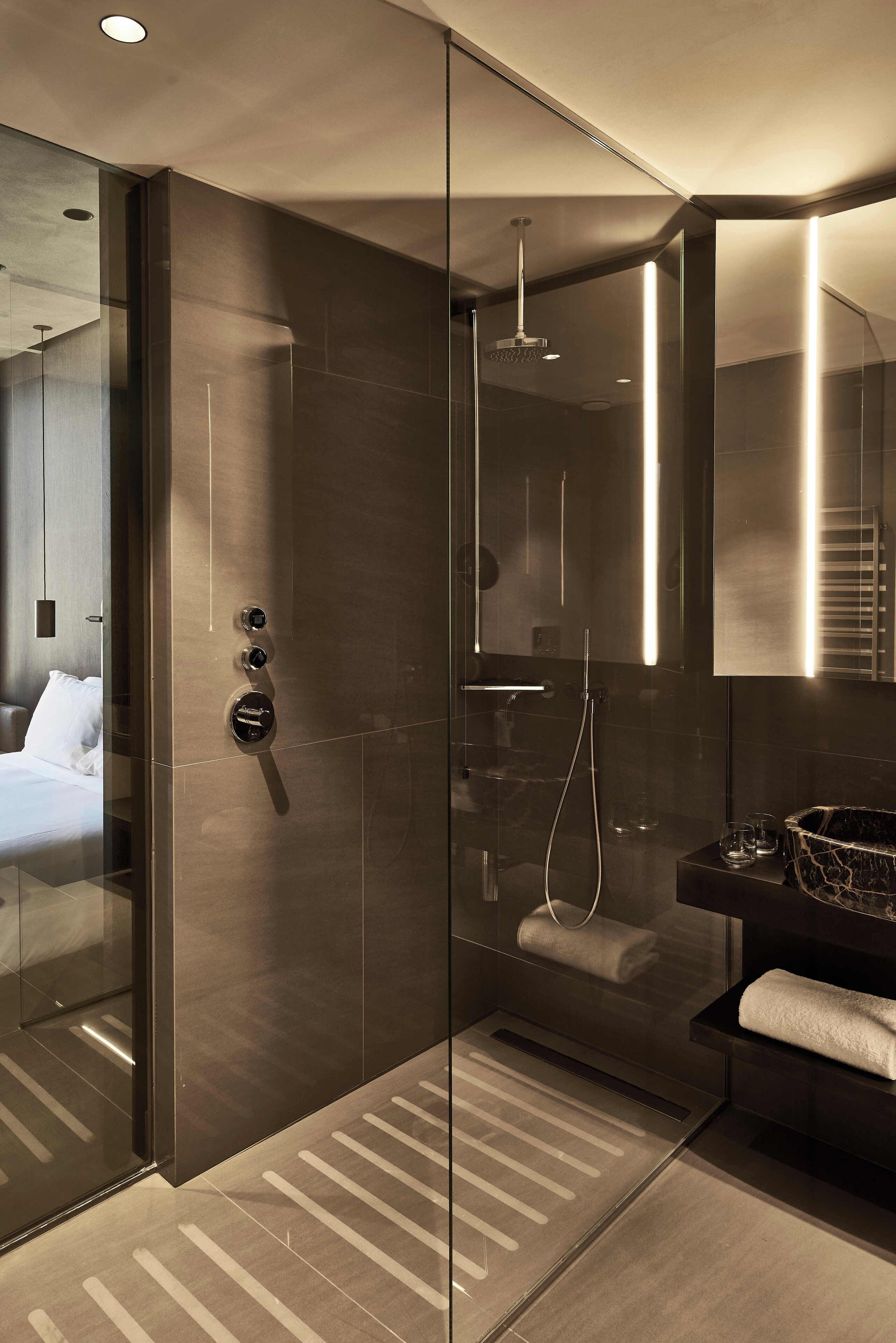 Een moderne hotelbadkamer met een douche met glazen wand, een grote spiegel en een zwart aanrechtblad met een handdoek.