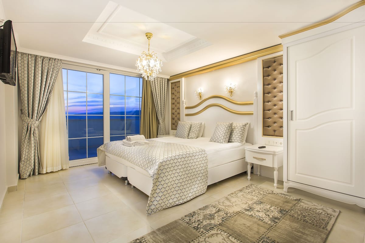 A bedroom with a large bed, a nightstand, a wardrobe, and a view of the sea through the window.