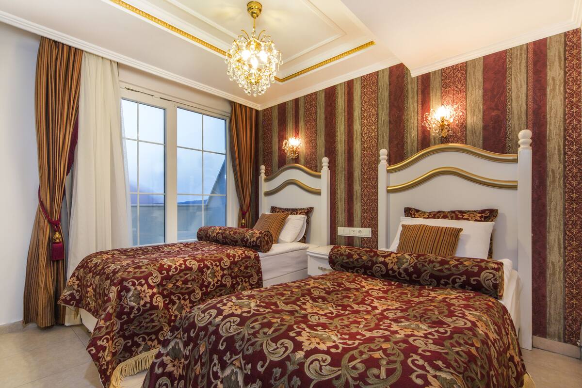 A hotel room with two beds, a chandelier, and a view of the sea.