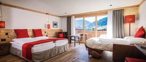 Habitación de hotel con una cama grande, una cama más pequeña, un sofá y una mesa. Se ve una vista de montañas a través de la ventana.
