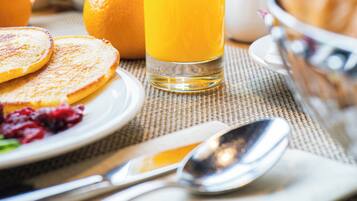 Desayuno con tortitas, zumo de naranja, cruasanes y un bol de fruta.
