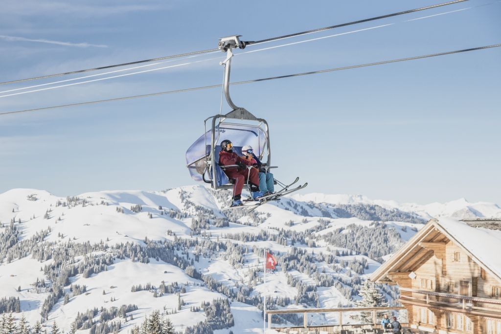 A ski lift with skiers, a wooden cabin, and a snowy mountain landscape.