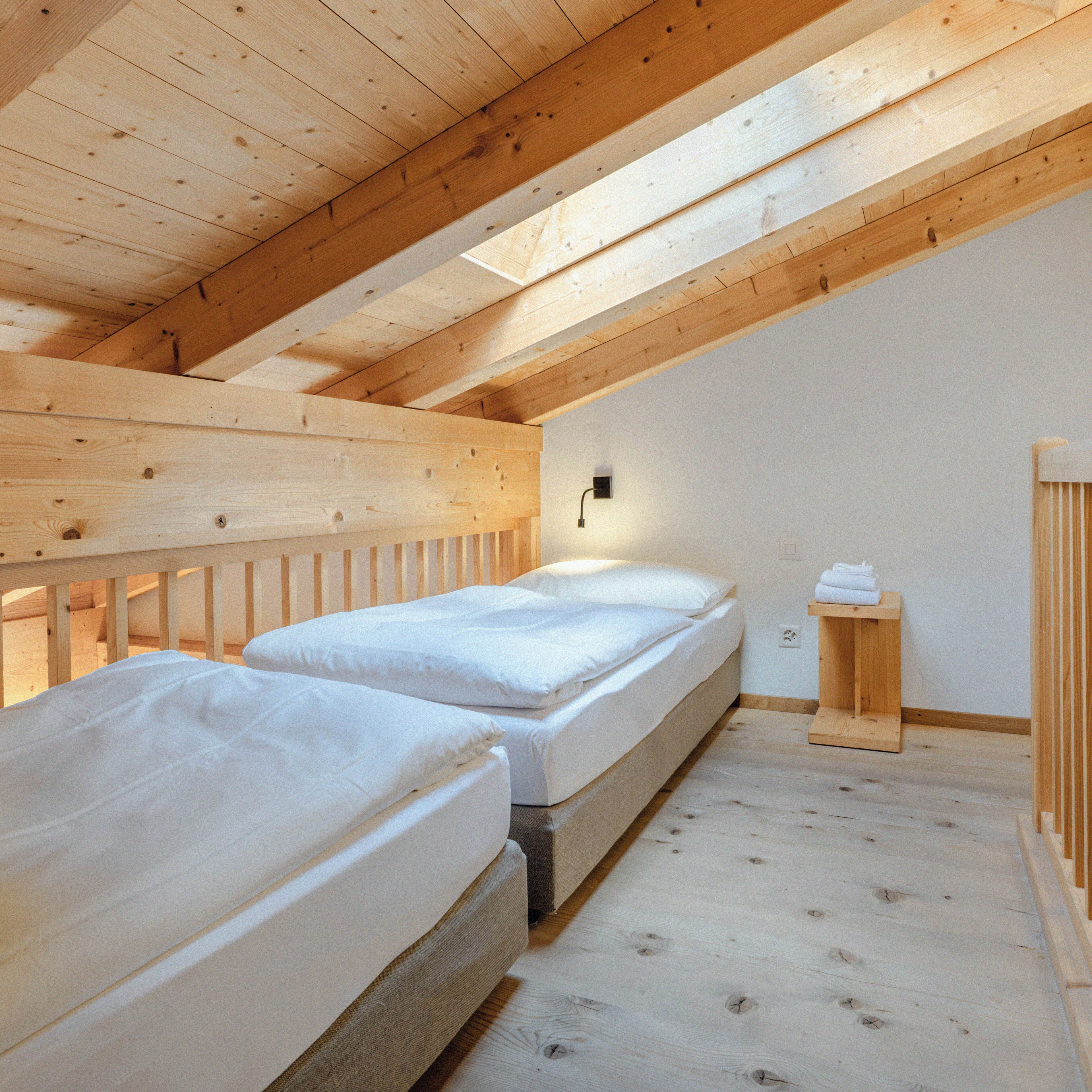 Una habitación con dos camas, vigas de madera, una mesita de noche y una lámpara fijada a la pared.