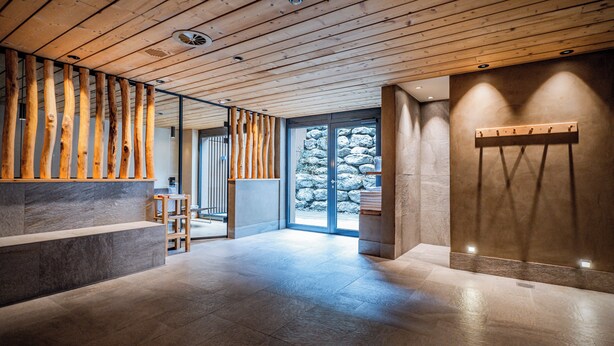 A modern interior with a wooden ceiling, stone walls, and a stone fireplace. - Hotel Spitzhorn (Saanen)