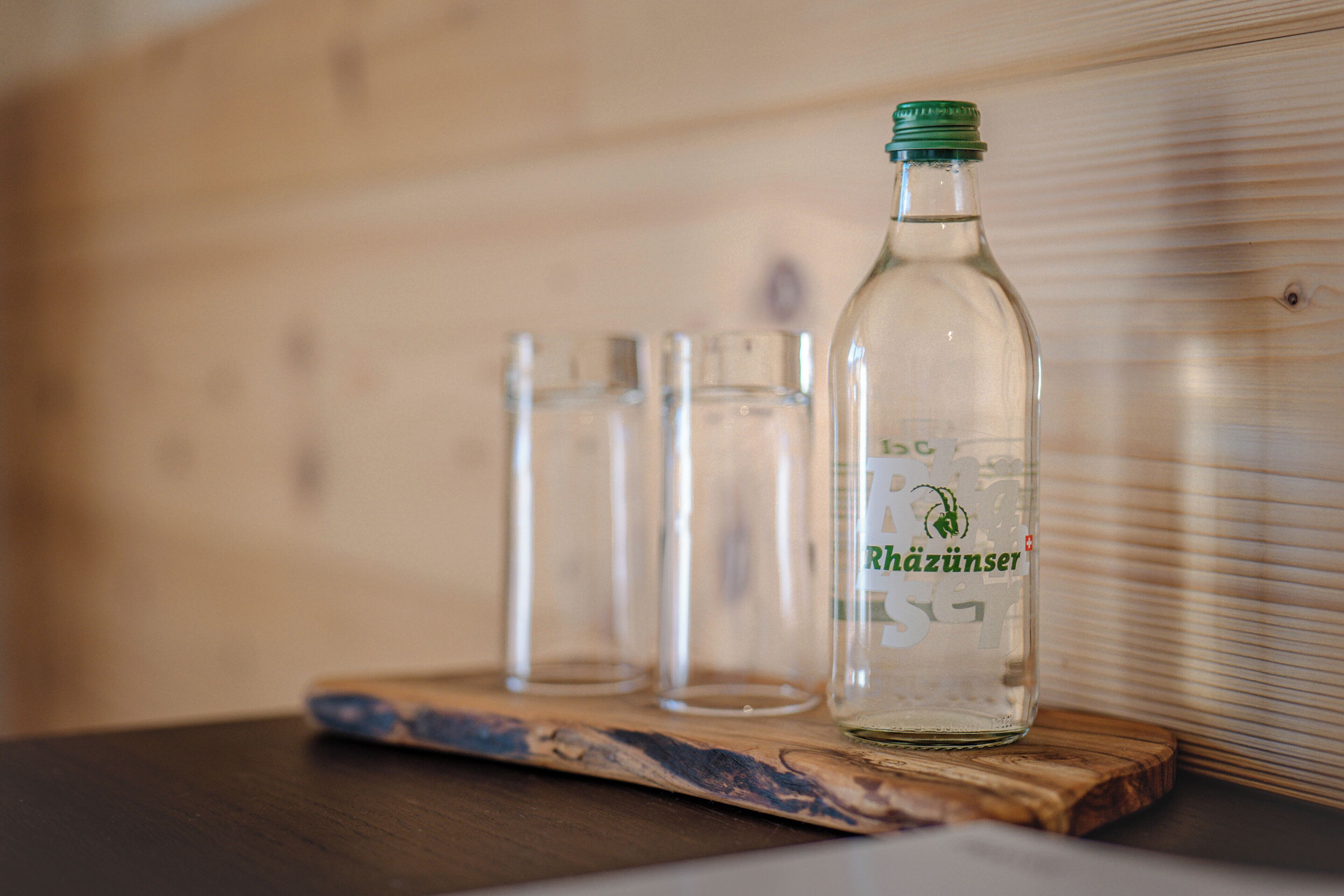 Una botella de vino Rhäzüns sobre una bandeja de madera con tres copas.