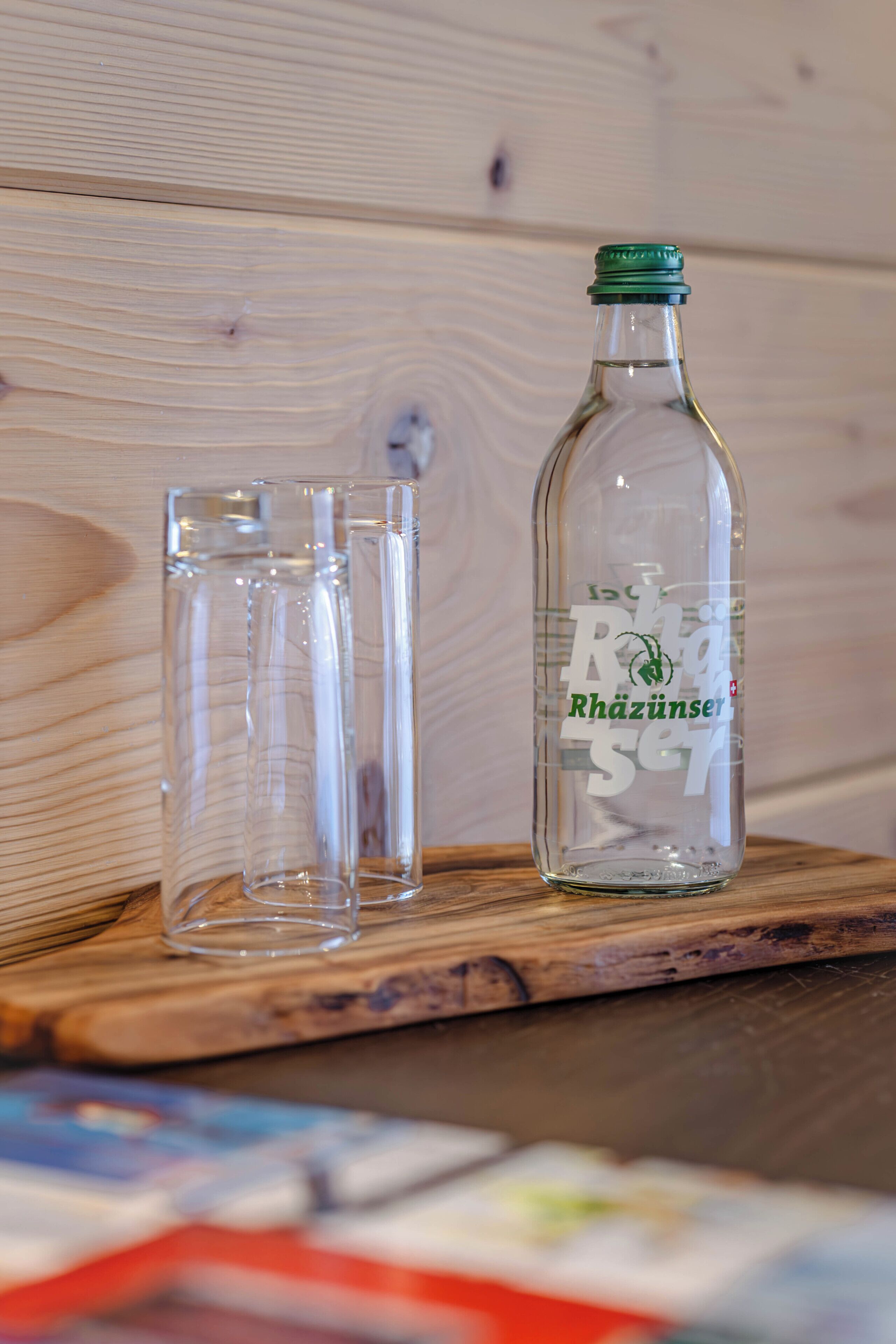 Una botella de vidrio transparente con tapa verde y etiqueta sobre superficie de madera.